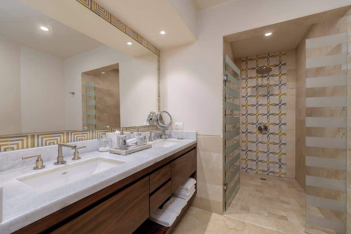 Un baño moderno con un espejo grande, dos lavamanos y una ducha con azulejos estampados.
