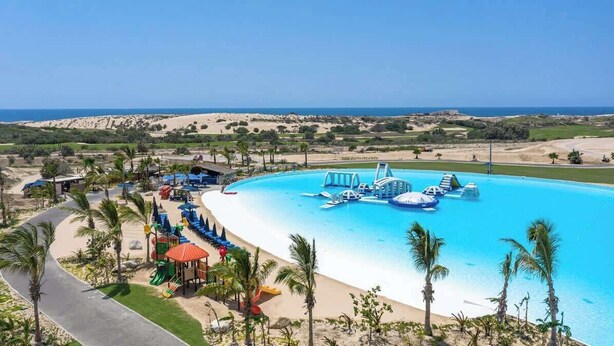 Un complexe hôtelier doté d’une grande piscine, de palmiers et offrant une vue sur la plage.