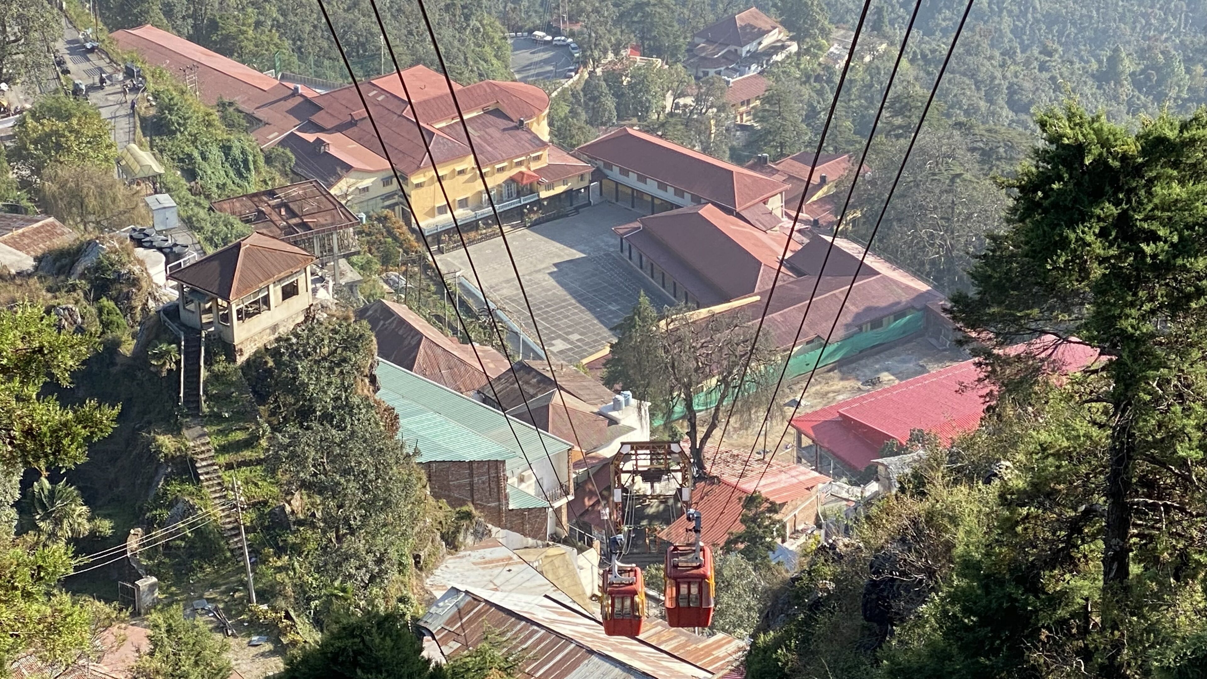 Un sistema de teleférico con cabinas suspendidas por cables, un edificio de techo rojo y vegetación circundante.