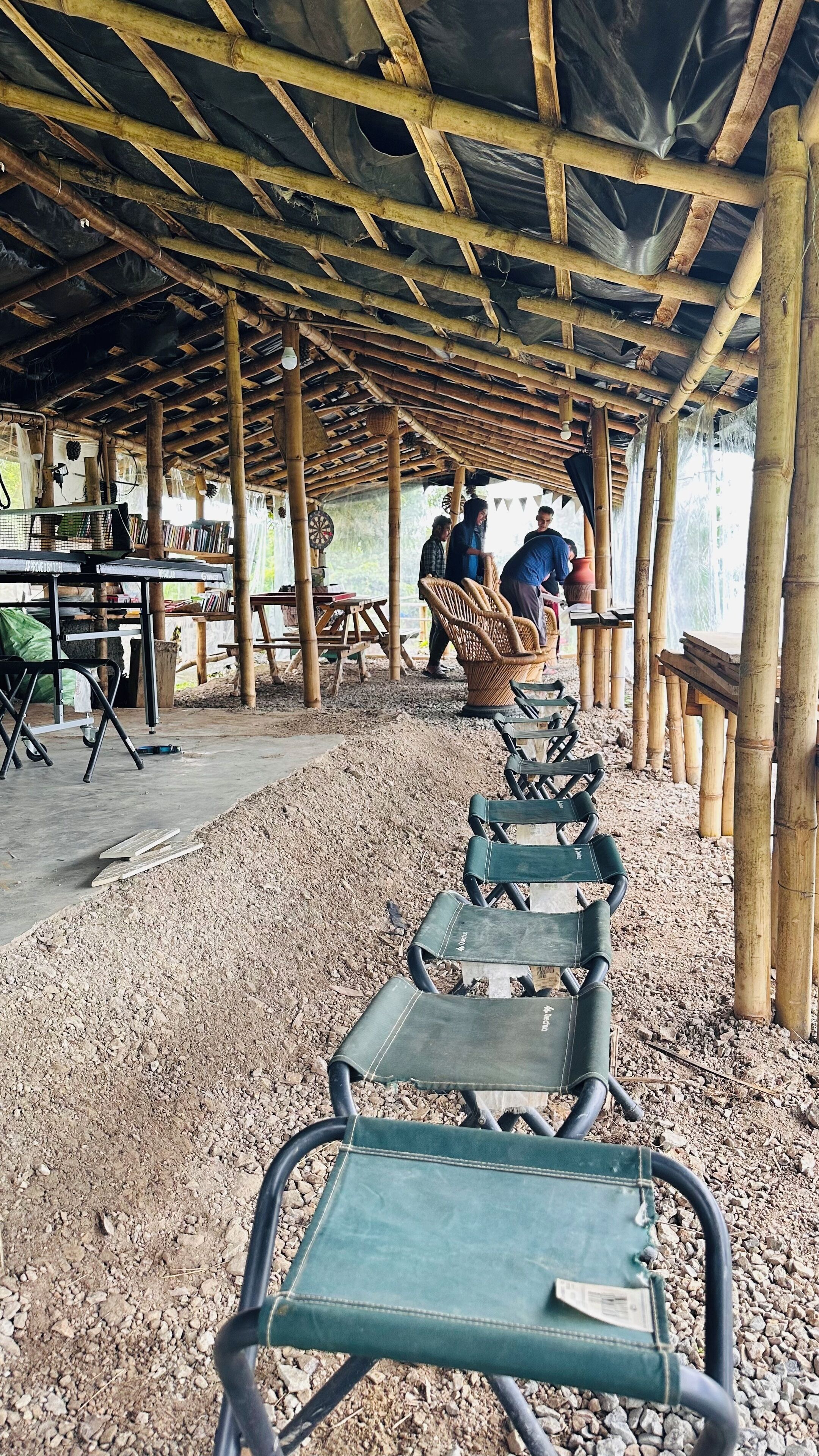 A covered outdoor seating area with bamboo poles and a gravel ground.