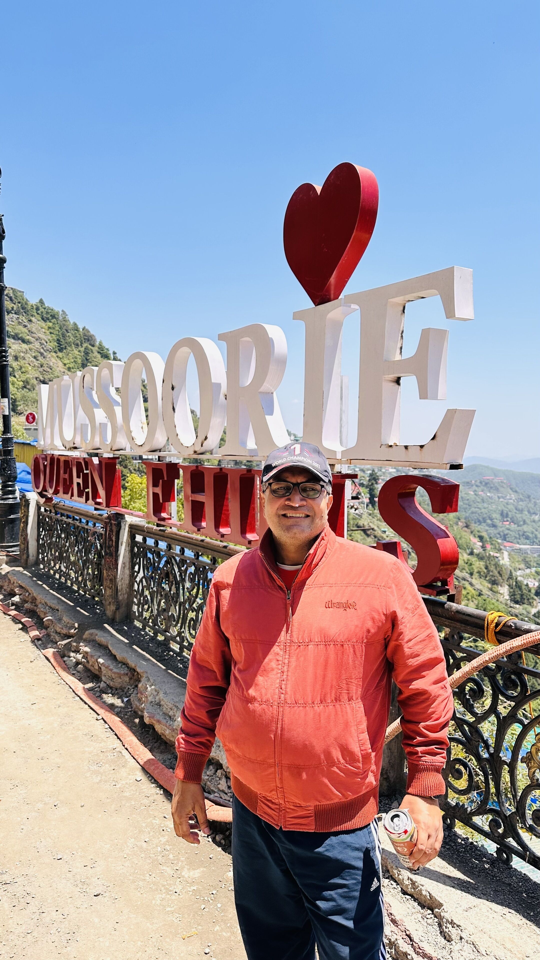 Une personne se tient devant un panneau sur lequel on peut lire : « MUSSOORIE QUEEN ET AL. »