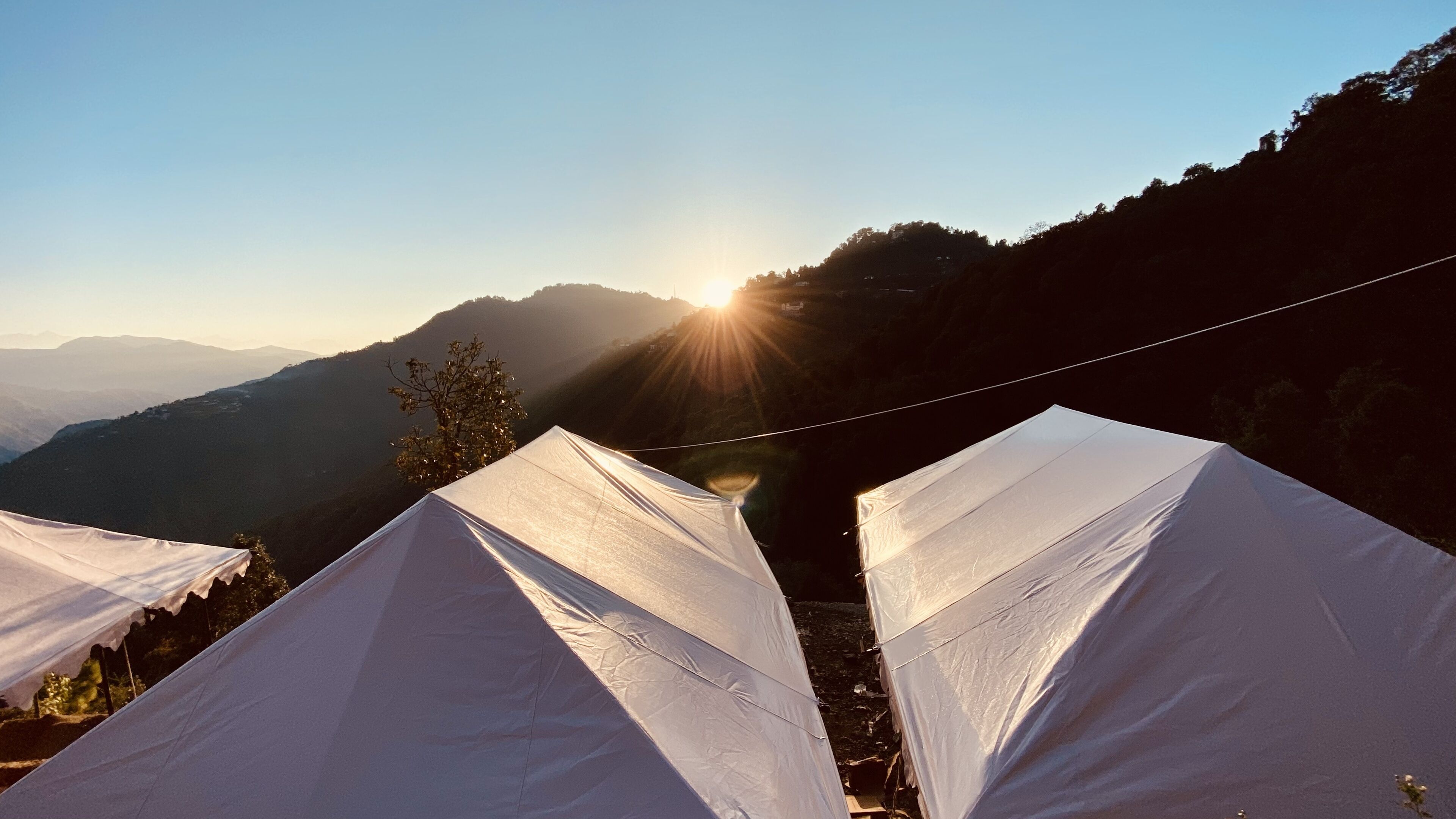 A campsite with tents set up on a hillside, overlooking a valley with mountains in the distance.