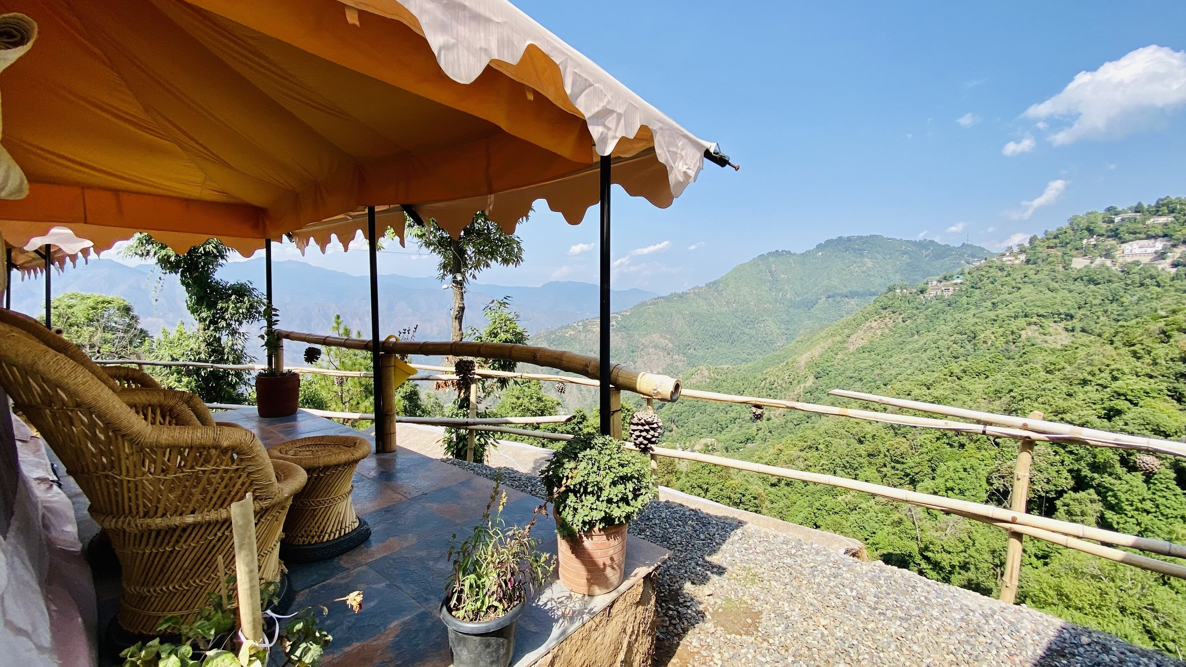 Una terraza con mobiliario de mimbre, plantas en macetas y vistas a un paisaje montañoso.