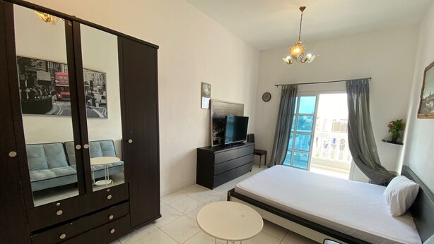 A bedroom with a bed, a TV, a dresser, a mirror, a sofa, and a small table. - Villa 125  (Dubai)