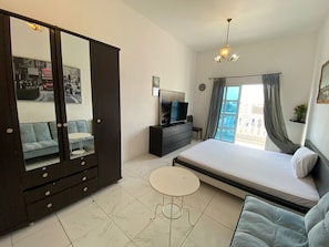 A bedroom with a bed, a TV, a dresser, a mirror, a sofa, and a small table. - Villa 125  (Dubai)