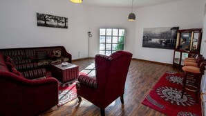 A living room with a sofa, armchair, and a coffee table. There is a window with a view of greenery and a painting on the wall. - Villa 125  (Dubai)