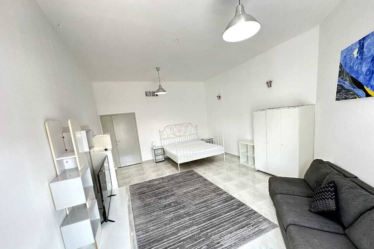 A modern, minimalist bedroom with a bed, bedside tables, a grey sofa, and a large window.
