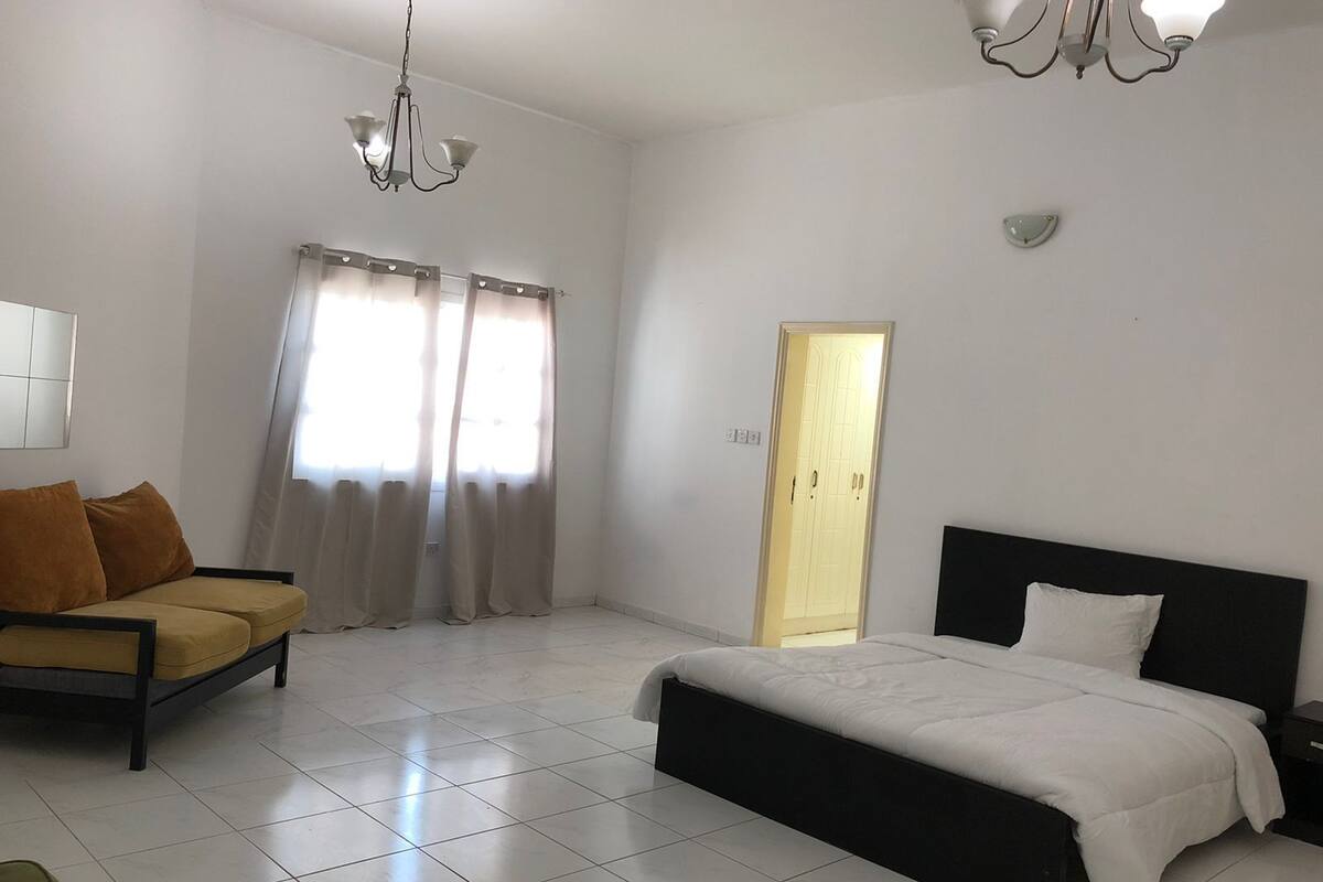 A bedroom with a bed, a sofa, a chandelier, and a door.