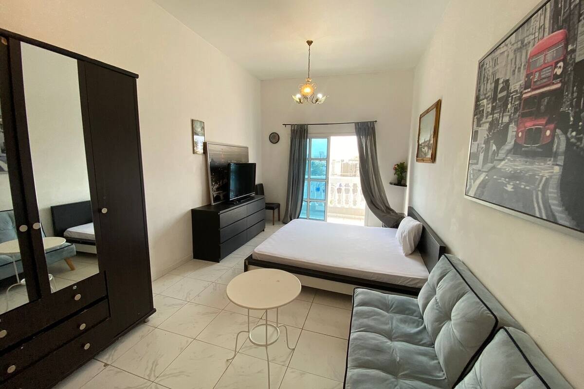 A bedroom with a bed, a sofa, a TV on a dresser, a mirror, and a balcony with a view.