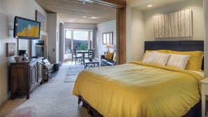 A bedroom with a large bed, a wooden headboard, a dining area with a table and chairs, and a view through a glass door to an outdoor area. - Pinnacle Place Ski-In/Out | Views, Fireplace, Covered Parking, Deck, Hot Tub (Durango)