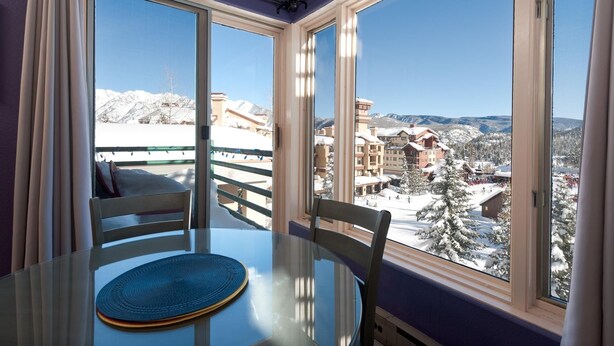 A room with a round glass table and chairs, large windows with a view of a snowy mountain and buildings. - Pinnacle Place Ski-In/Out | Views, Fireplace, Covered Parking, Deck, Hot Tub (Durango)