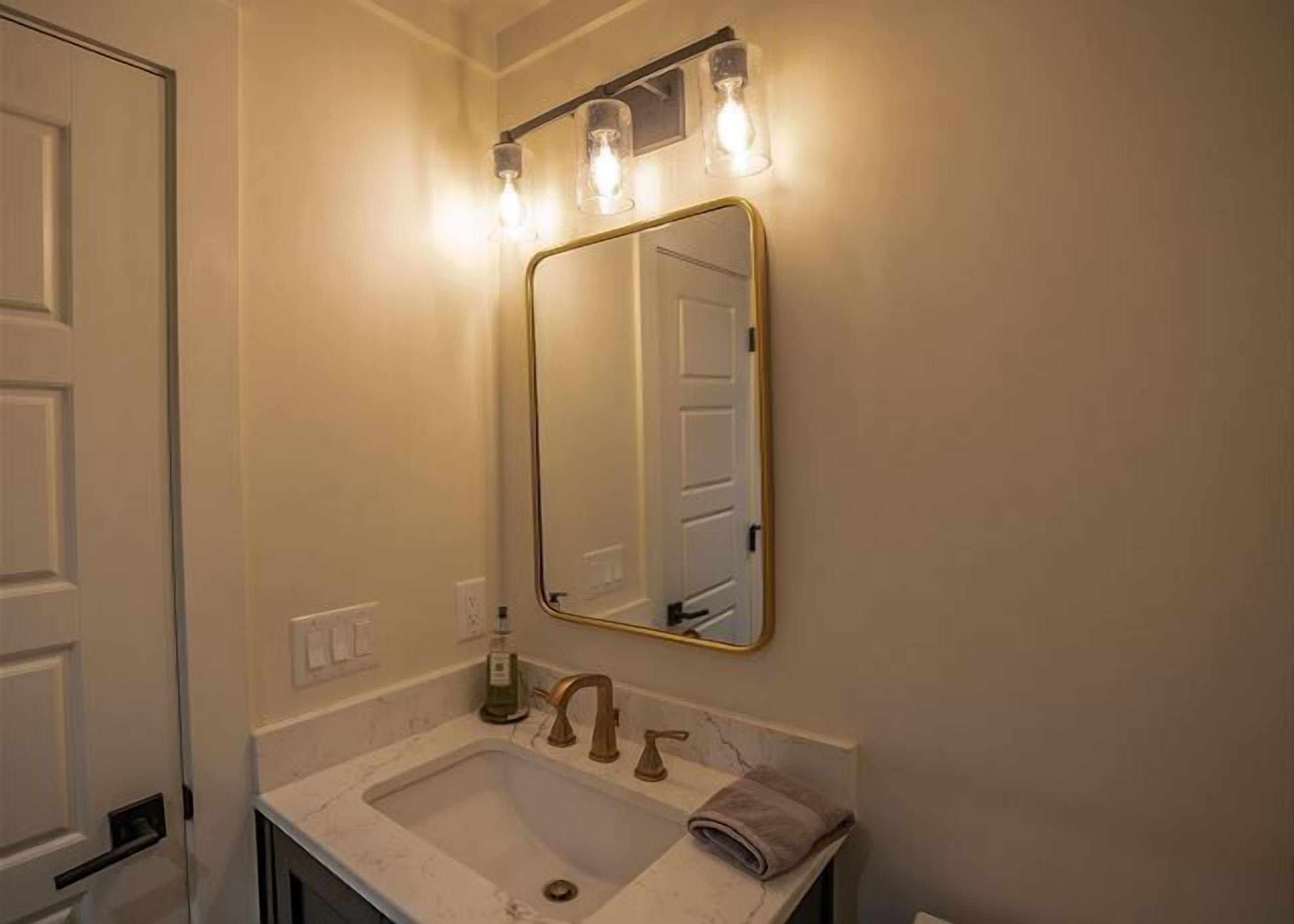 A bathroom with a sink, mirror, and three wall-mounted lights.