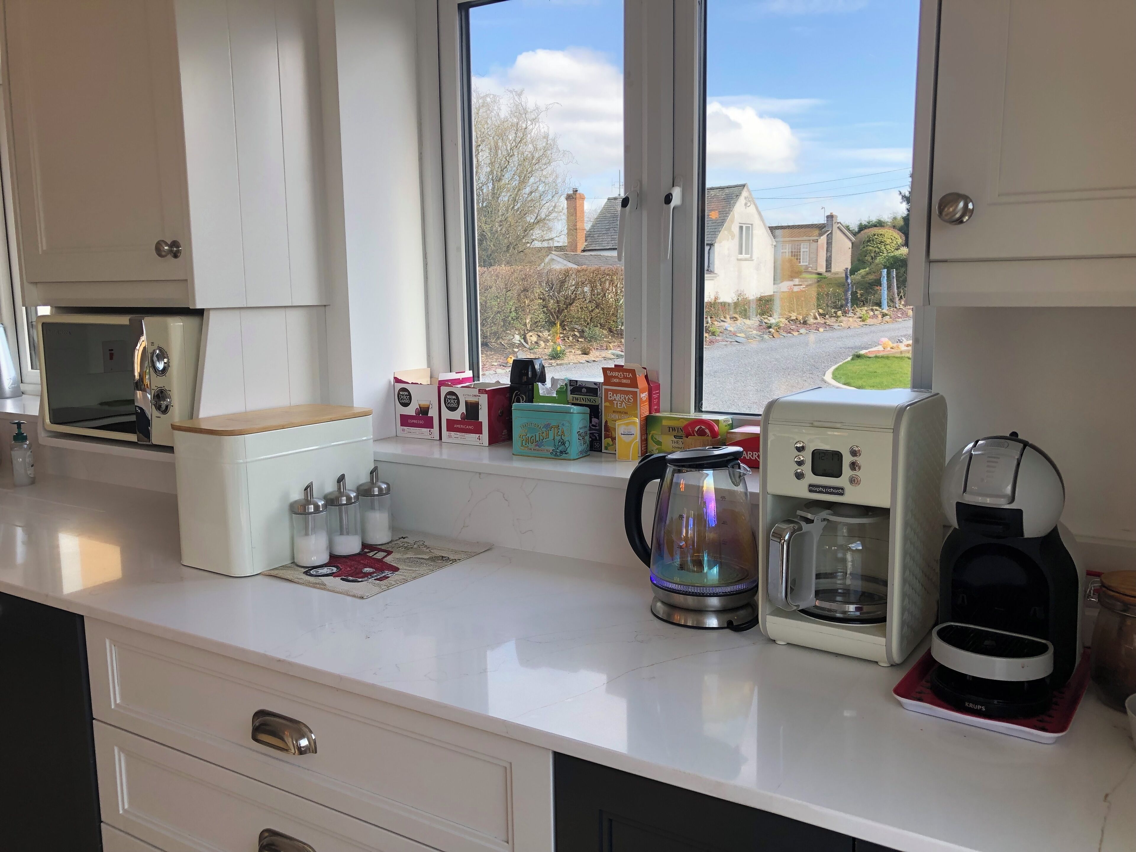 A kitchen with a window view, a coffee maker, a kettle, and various tea boxes.