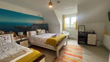A bedroom with two beds, a desk, a chair, a radiator, and a window with curtains.