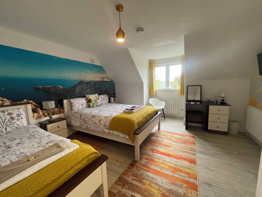 A bedroom with two beds, a desk, a chair, a radiator, and a window with curtains.