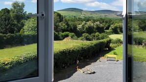 A room with a large window offering a view of a green landscape with hills and a clear sky.