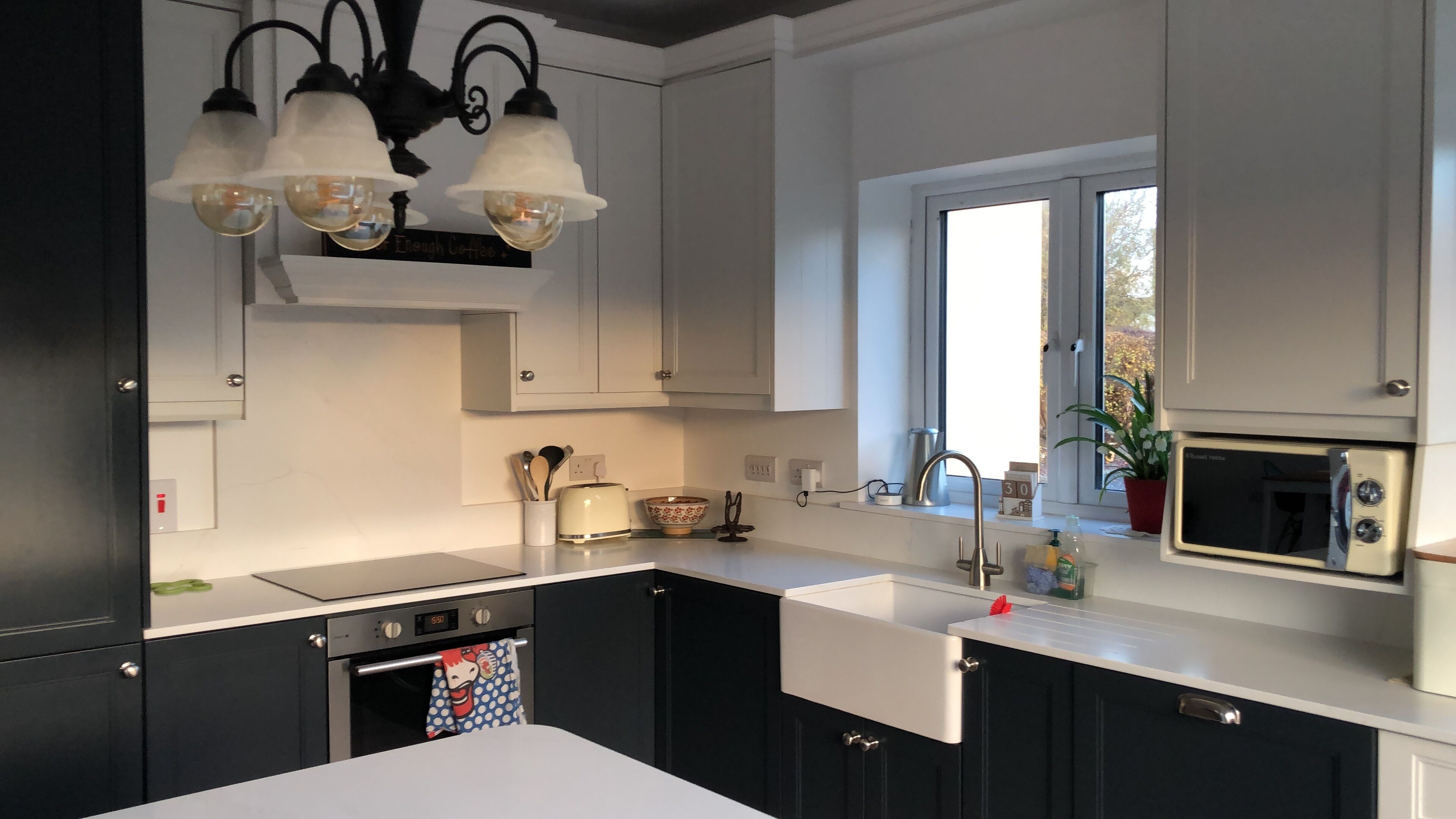 A modern kitchen with black cabinets, a white countertop, a built-in oven, a microwave, and a window providing natural light.