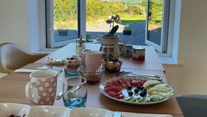 A dining table with a view of the countryside through open windows.