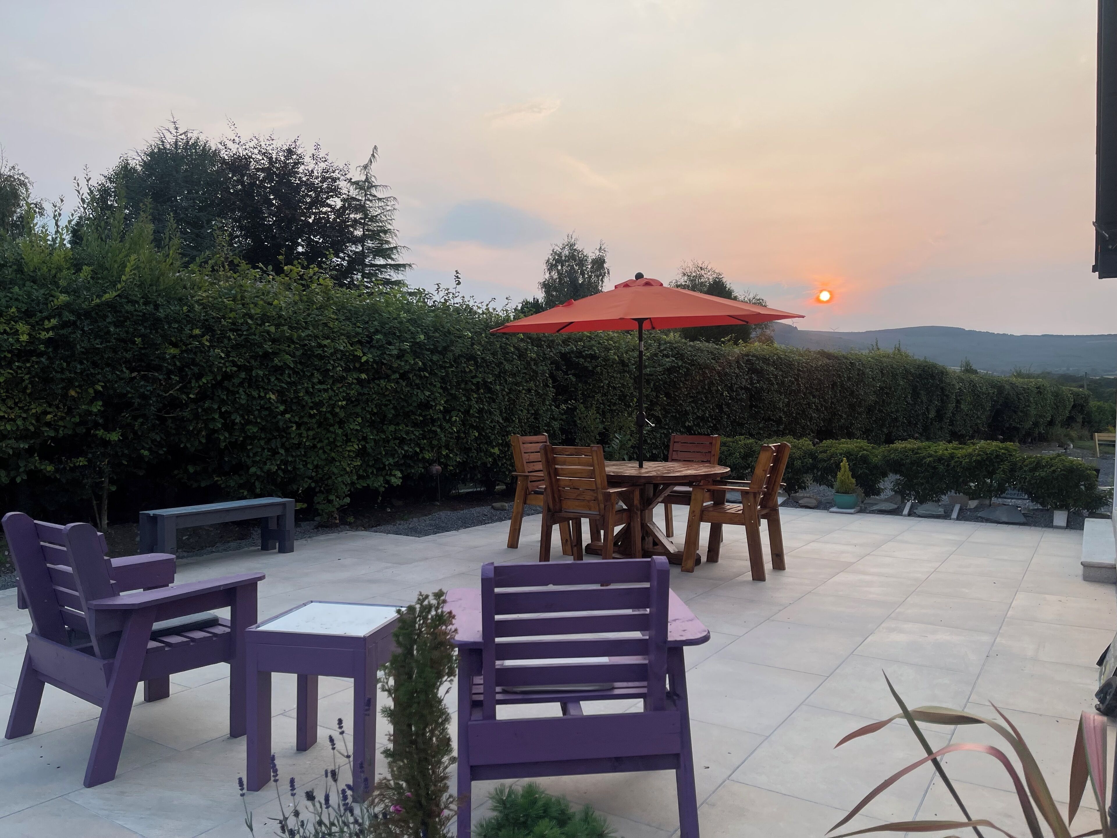 An outdoor patio with a round table and chairs, a purple bench, and a red umbrella.