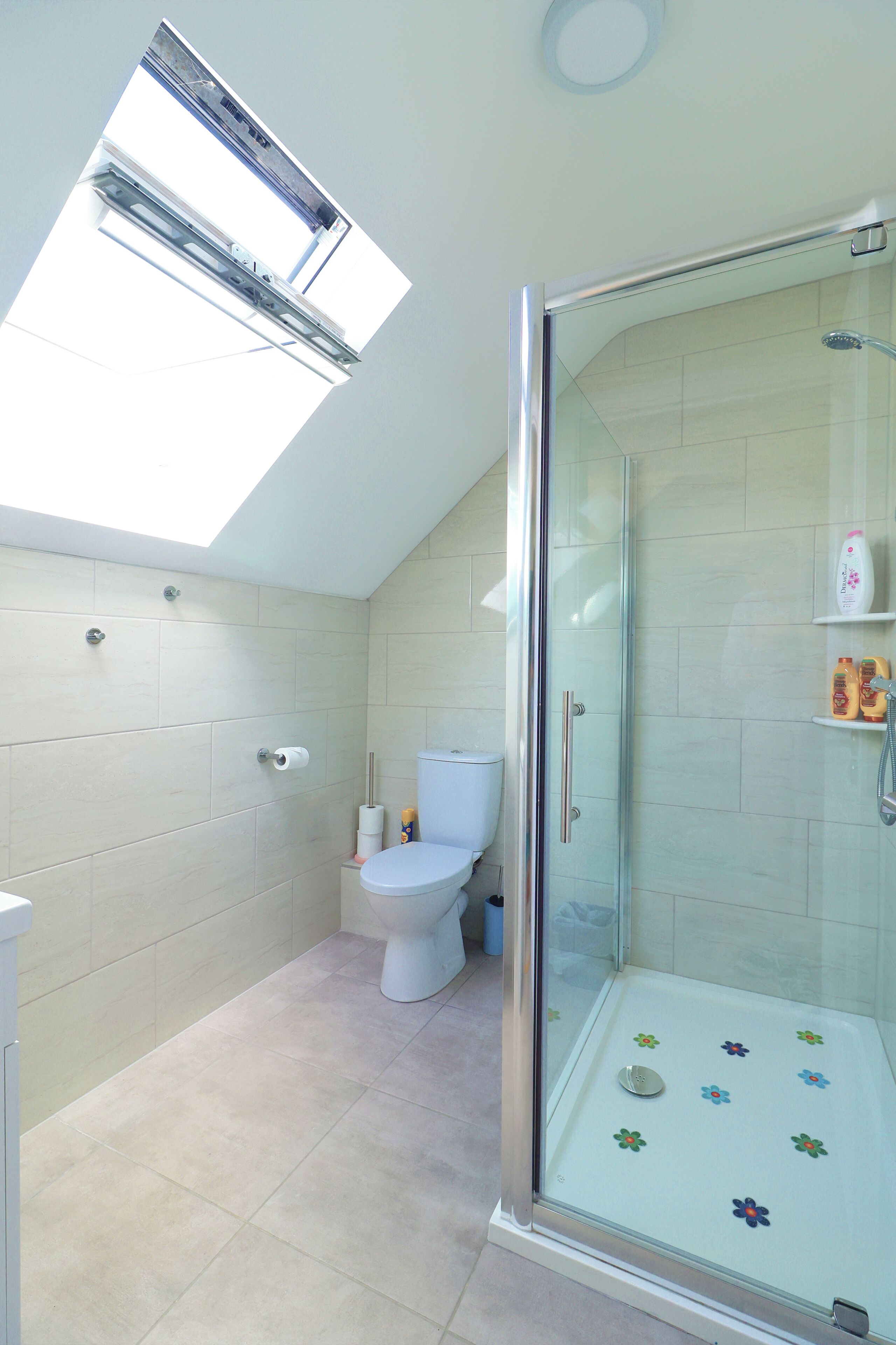 Un baño con tragaluz, inodoro, ducha con puerta de vidrio y paredes de azulejos.