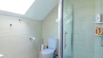 Un baño con tragaluz, inodoro, ducha con puerta de vidrio y paredes de azulejos.