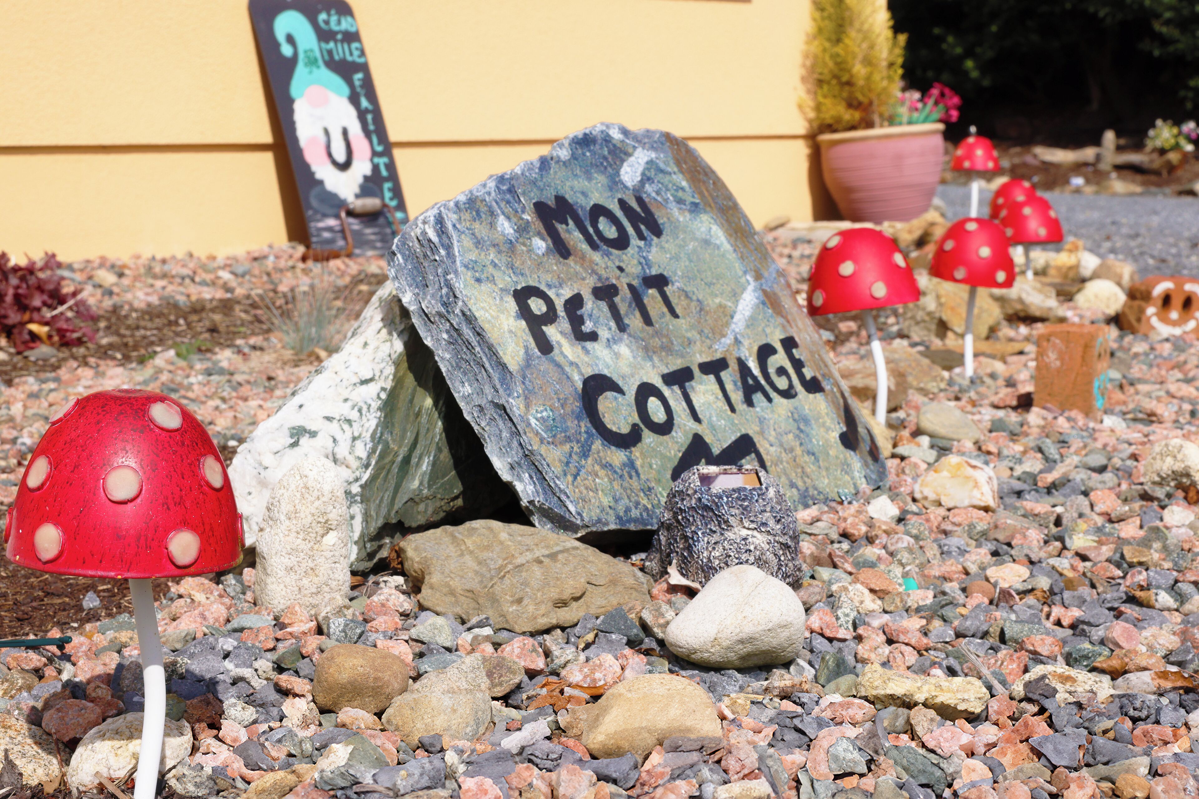 Un rocher sur lequel est inscrit « Mon Petit COTTAGE », entouré de petits galets et de champignons décoratifs.