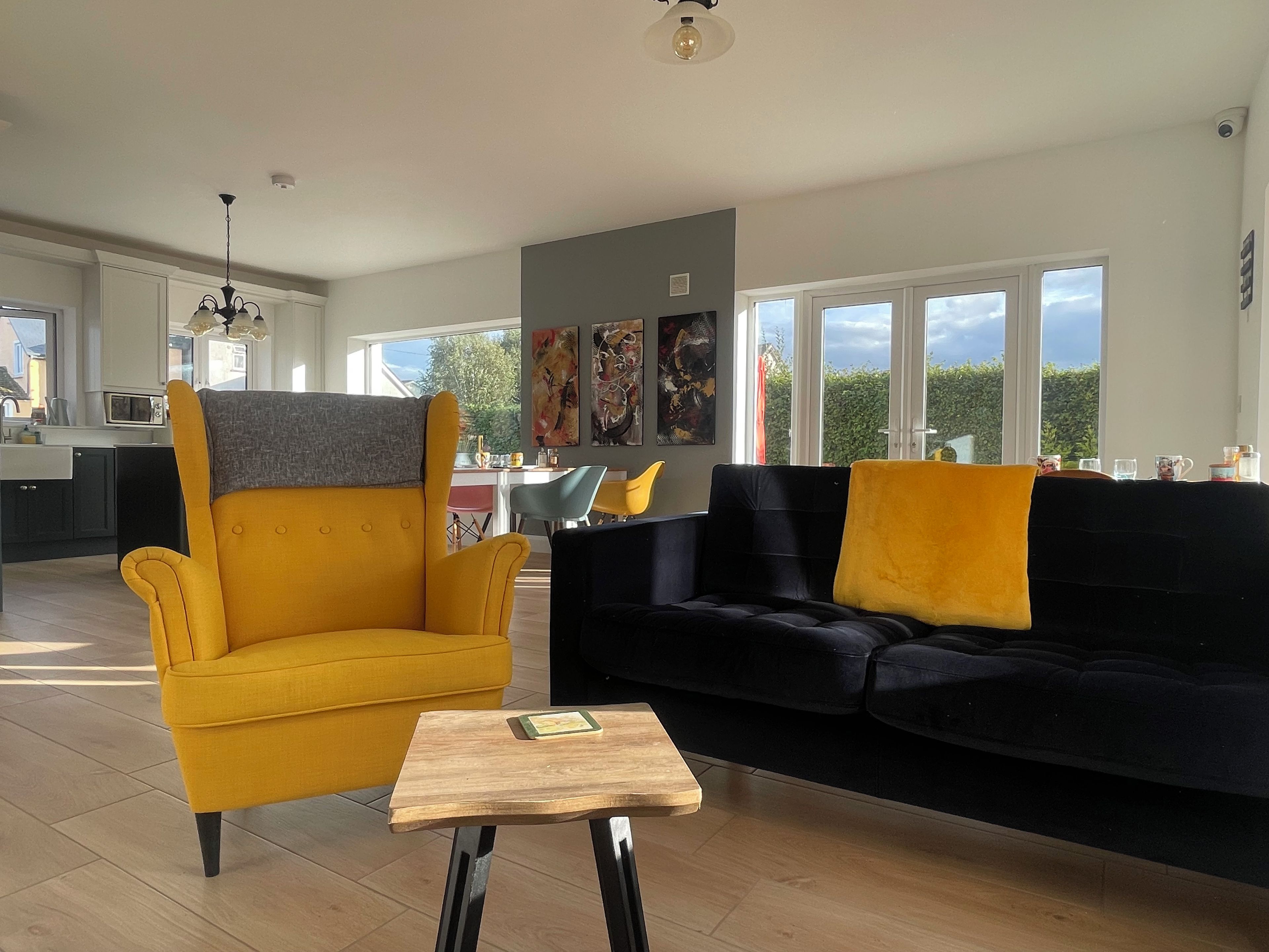 A modern living room with a yellow armchair, a black sofa, and a wooden coffee table.