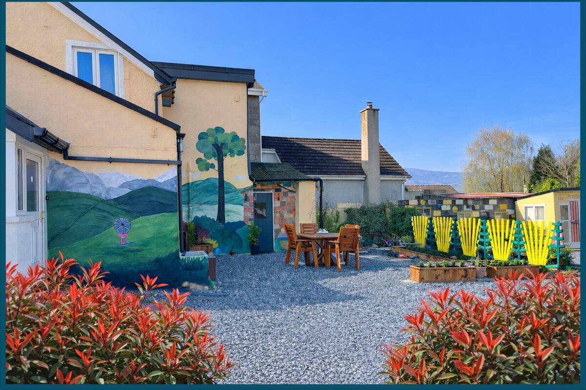 A house with a painted mural, a gravel patio, and a garden with red foliage.