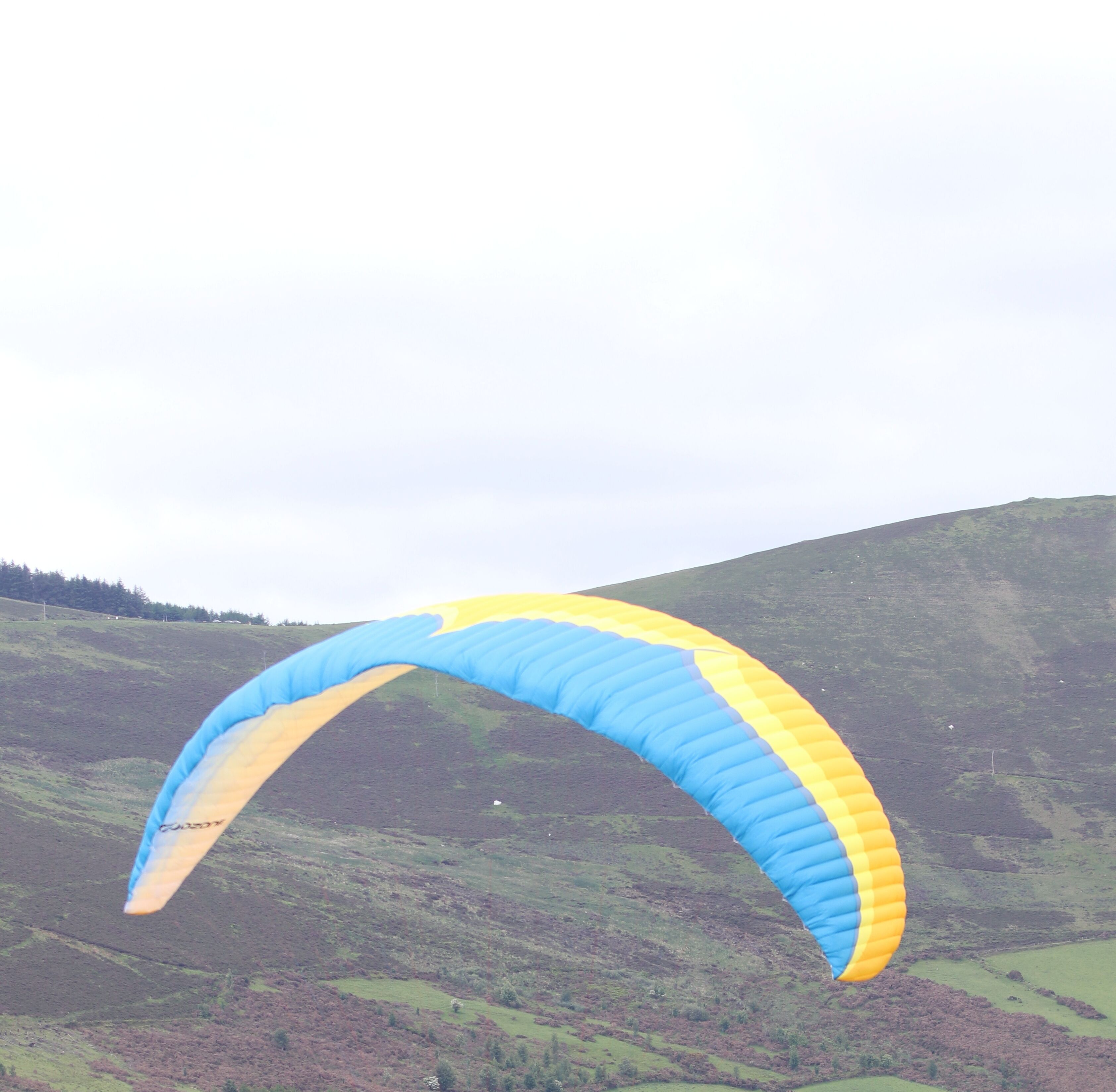 Un parapente con una vela azul y amarilla sobre un paisaje montañoso.