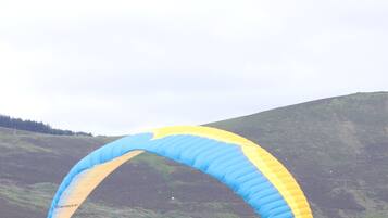 Un parapente con una vela azul y amarilla sobre un paisaje montañoso.