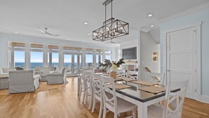 Uma sala de estar espaçosa com uma mesa de jantar, cadeiras brancas e vista para o mar.