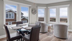 Un coin repas avec une table en verre, des fauteuils en cuir et une vue sur la plage grâce à de grandes fenêtres.