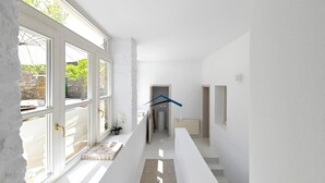 Ein heller Korridor mit großen Fenstern, einer Treppe und einer zur Toilette führenden Tür.