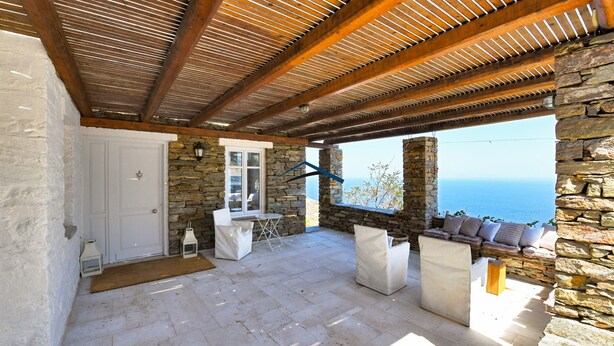 Eine Terrasse mit Steinwänden, Holzboden und einer Sitzgruppe mit Kissen.