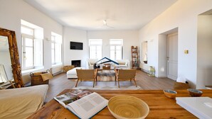 Ein großzügiges Wohnzimmer mit Holzboden, einem großen Spiegel, einer Couch, zwei Sesseln, einem Couchtisch und einem Bücherregal.