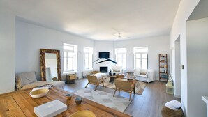 Ein geräumiges Wohnzimmer mit einem Holzessttisch, zwei weißen Sofas, einem großen Spiegel und einem Deckenventilator.