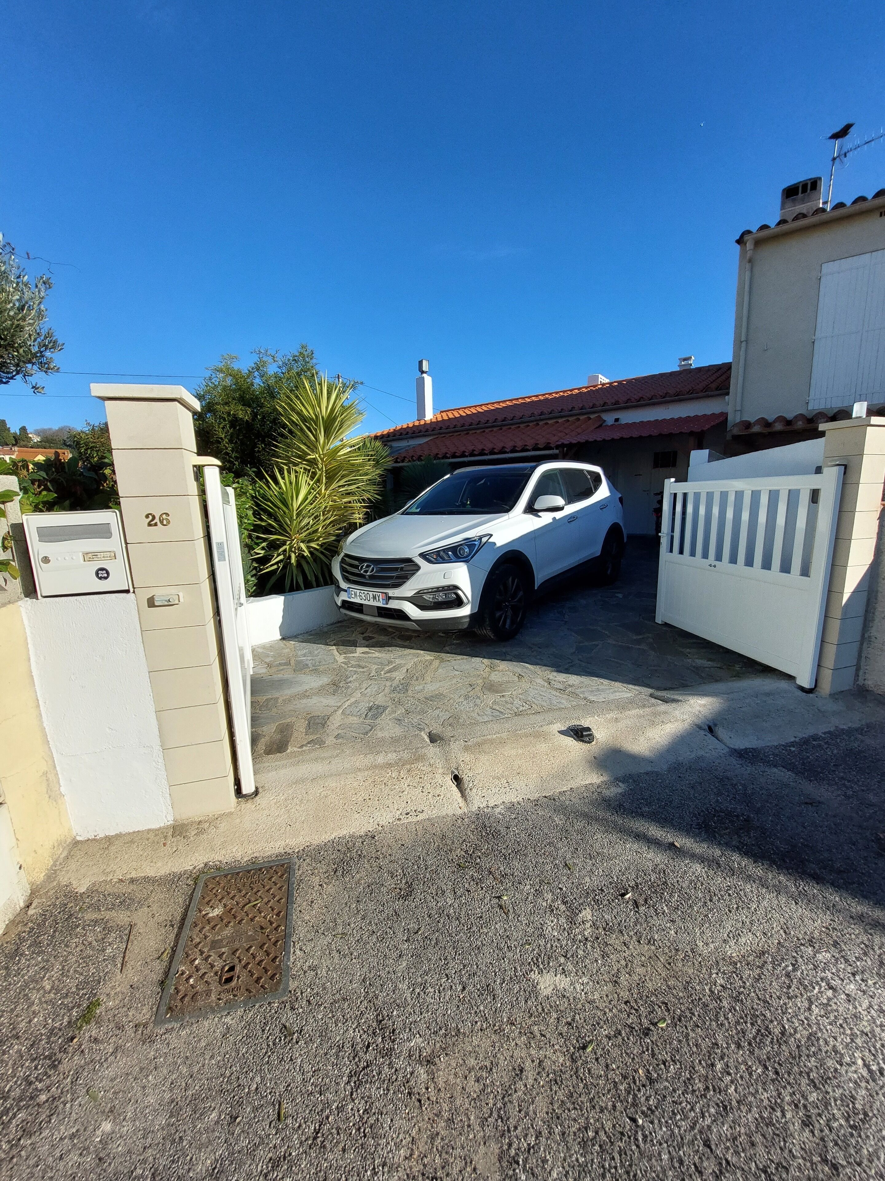 A white car parked in a gated driveway with a building in the background.