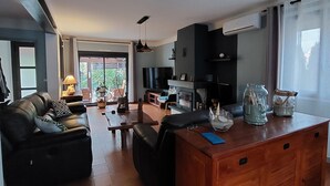 Un salon moderne avec un canapé, une table basse et un îlot en bois doté de tiroirs. On aperçoit un téléviseur et une cheminée au fond.