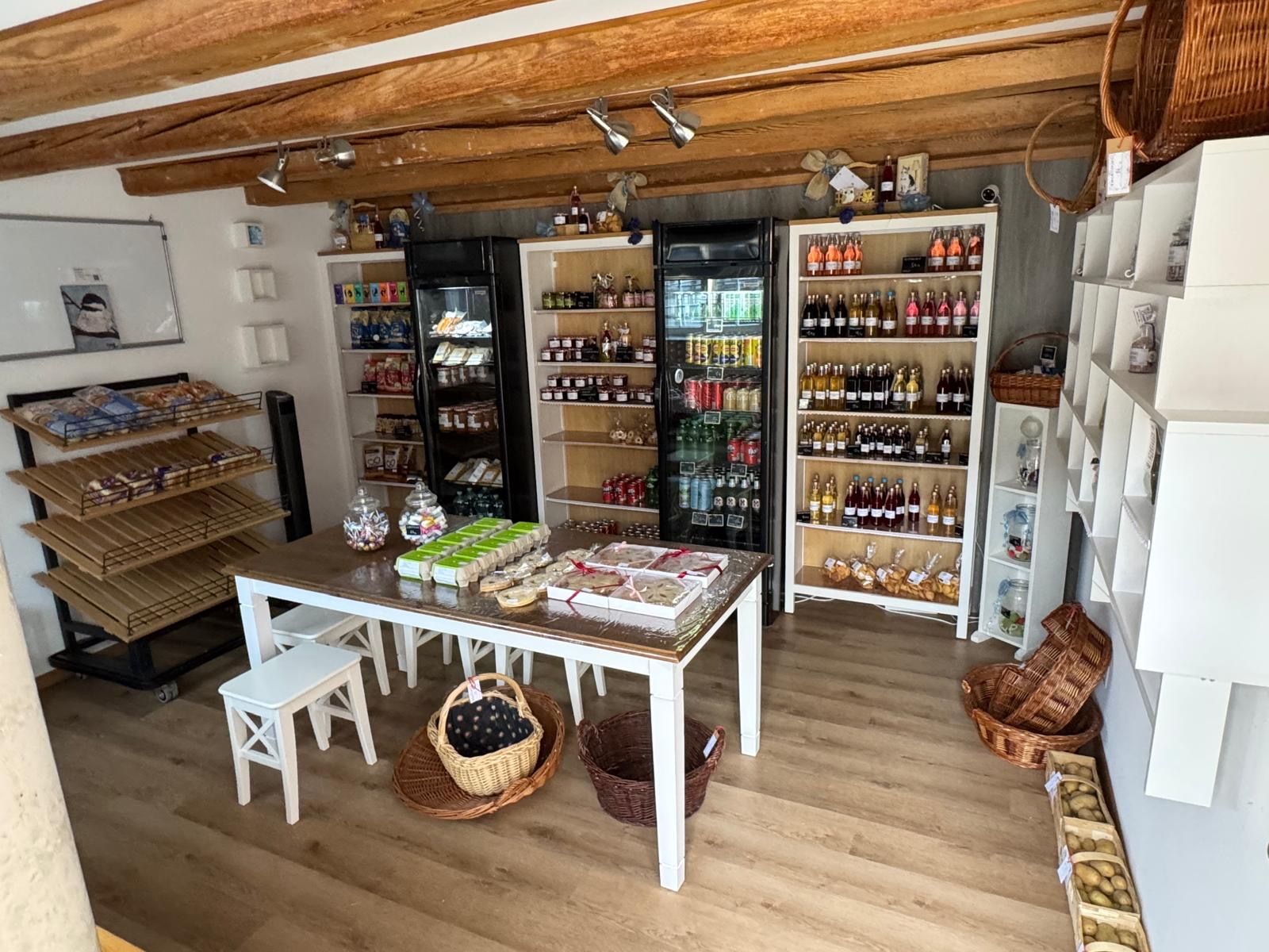 Un magasin dont les étagères sont remplies de divers produits, une table où sont disposés des articles emballés, et des paniers posés sur le sol.