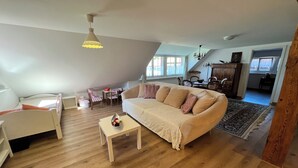 A loft-style living room with a high ceiling, a white sofa, a small table, and a dining area with a table and chairs. - Idyllischer Bauernhof 1 (Wildensbuch)