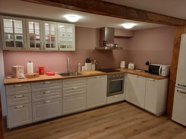 A compact kitchen with white cabinets, a wooden countertop, a sink, a stove, and a microwave. - Idyllic Farm 1 (Wildensbuch)