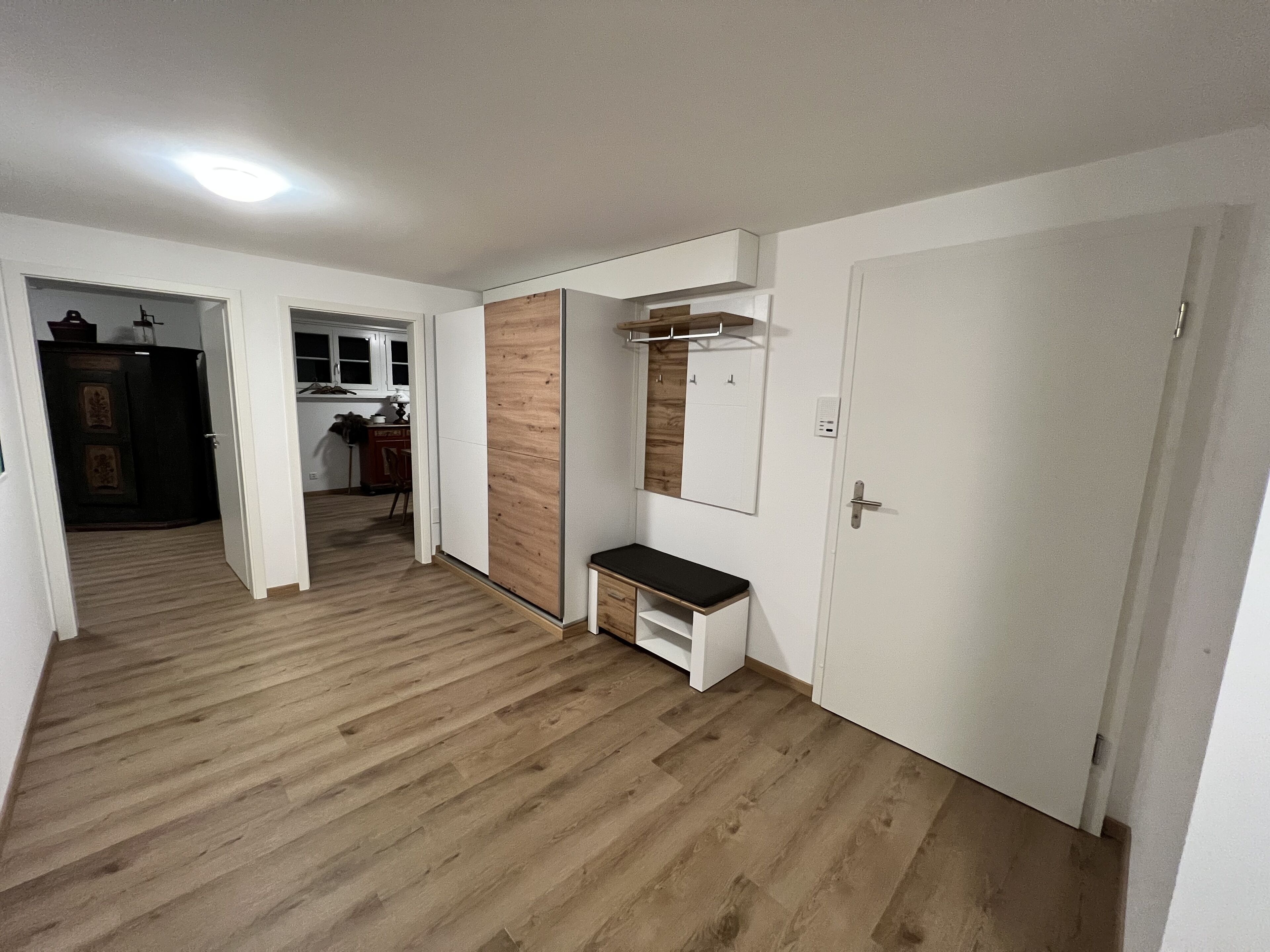 Ein Flur mit Holzboden, einer Bank, einem Spiegel und einer Tür.