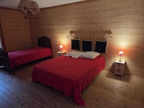 A room with two beds, each with a red bedspread, wooden walls, and bedside lamps.