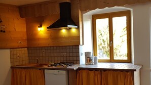 A kitchen with a gas stove, a coffee maker, and a window with a view of greenery. - Authentic Jura farmhouse at the gateway to the Cascades du Hérisson (Saugeot)