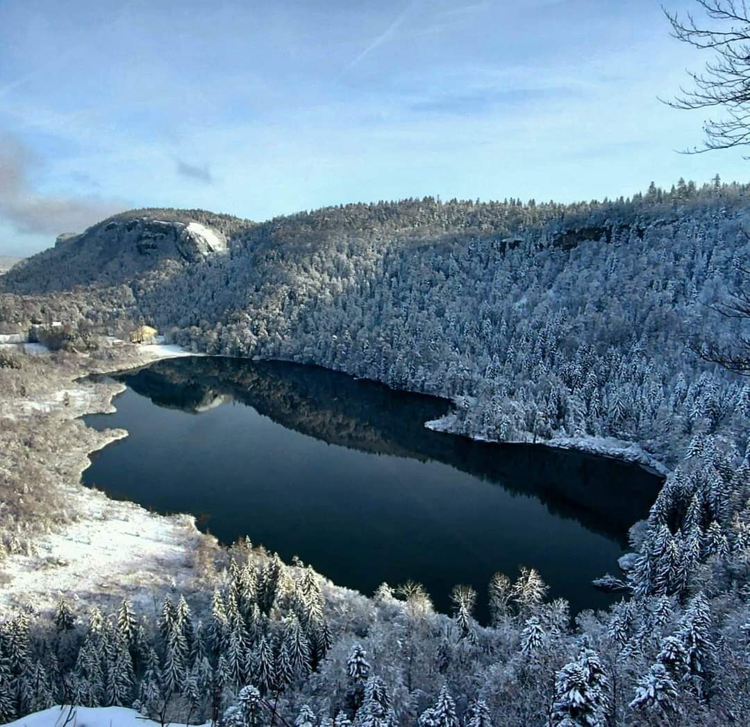 Un paisaje invernal tranquilo con un lago helado rodeado de árboles y colinas cubiertas de nieve.