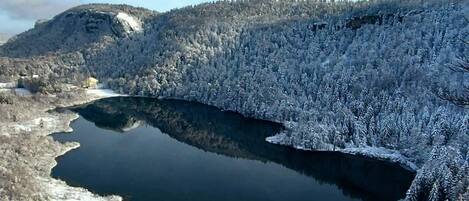 Un paisaje invernal tranquilo con un lago helado rodeado de árboles y colinas cubiertas de nieve.