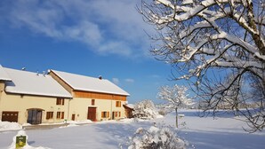 A snow-covered house with a sloped roof and a chimney, surrounded by snow-laden trees and a clear blue sky. - Authentic Jura farmhouse at the gateway to the Cascades du Hérisson (Saugeot)