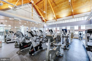 Une salle de sport équipée de divers appareils d’exercice, dotée d’un haut plafond en bois et de grandes fenêtres.