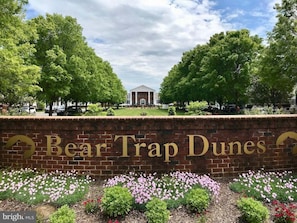 Un muro de ladrillo con señalización 'Bear Trap Dunes', rodeado de follaje y un cielo despejado.
