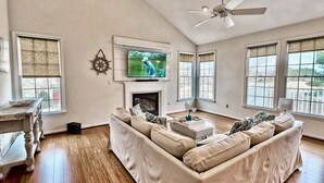 A living room with a sofa, television, fireplace, and large windows. - Bear Trap Dunes * 4BR Luxury townhouse (Ocean View)